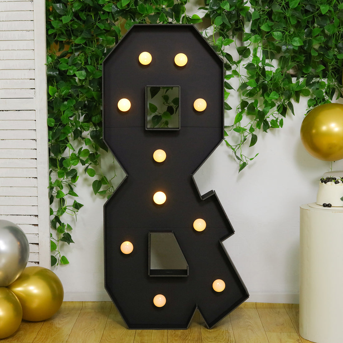 Black marquee number 8 with lights, set against greenery and gold balloons.