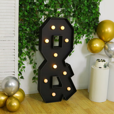 Large decorative number 8 light sign with bulbs, surrounded by greenery and balloons.