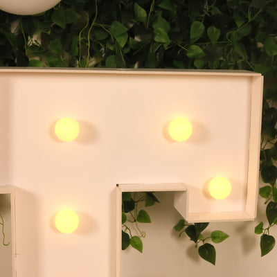 Light-up decorative letter with bulbs on a green wall.