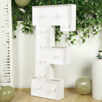 White marquee letter "F" with light bulbs, styled with greenery and balloons.