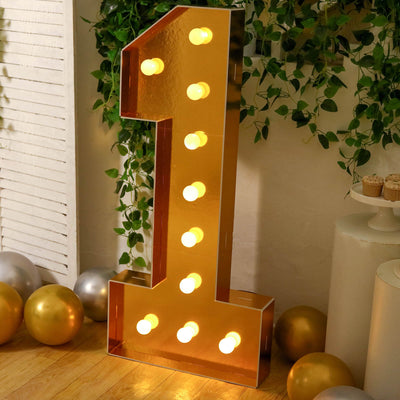 Gold marquee number 1 light with bulbs, balloons, and greenery
