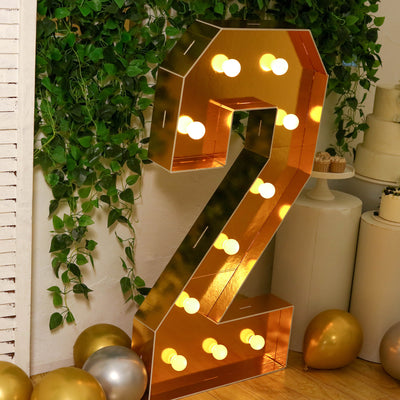 Illuminated marquee number 2 with bulbs, surrounded by greenery and festive balloons.