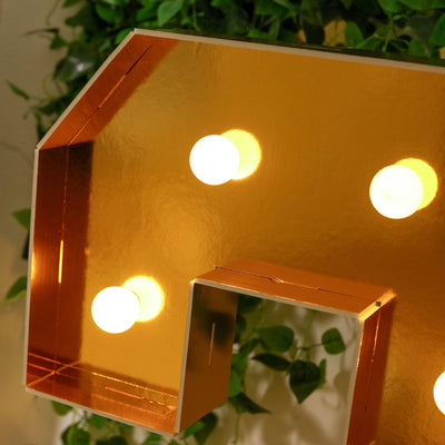 Gold letter light with bulbs against green foliage backdrop.