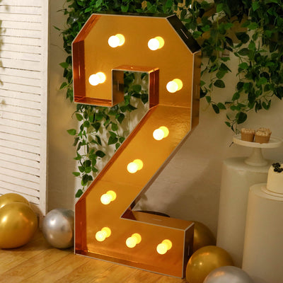 Gold illuminated number 2 marquee sign with balloons and greenery backdrop