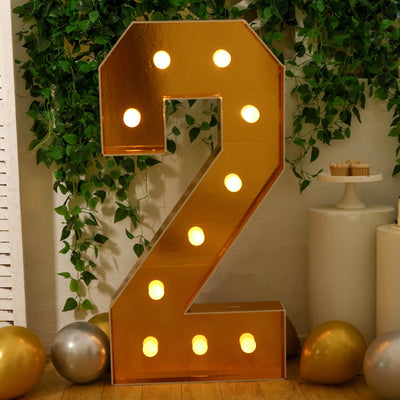 Gold marquee number two decoration with lights and greenery backdrop.
