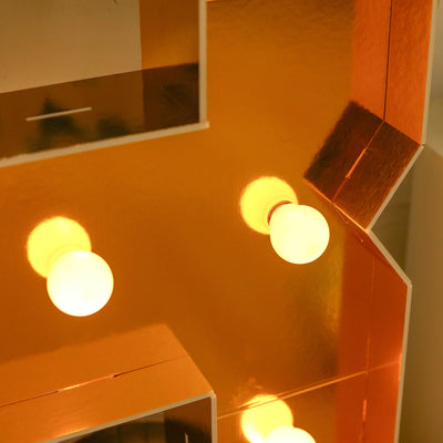 Gold marquee letter with glowing bulbs.