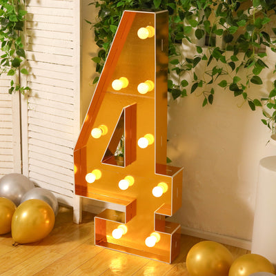 Gold marquee number 4 with lights, surrounded by balloons and greenery.