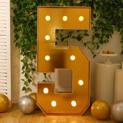 Gold marquee number 5 with lights, surrounded by balloons and greenery.