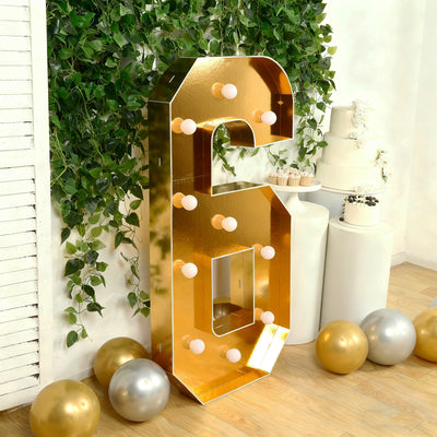 Gold marquee number six with lights, surrounded by balloons and greenery.