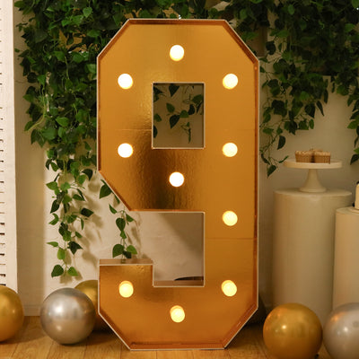 Gold marquee number 9 with lights, surrounded by greenery and decor elements.
