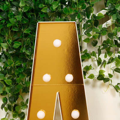 Gold letter "A" marquee sign with light bulbs against greenery backdrop.