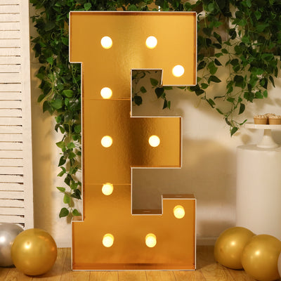 Gold marquee letter "E" with lights, surrounded by greenery and balloons.