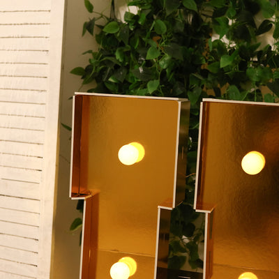 Gold marquee letters with bulbs, partially obscured by greenery.