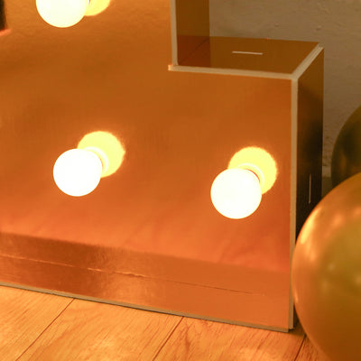 Gold marquee letter with glowing bulbs and decorative balloons.