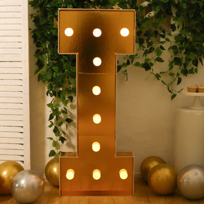 Gold marquee letter "I" with lights, surrounded by balloons and greenery.