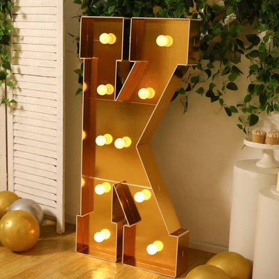 Gold marquee letter "K" with lights in a festive setting.