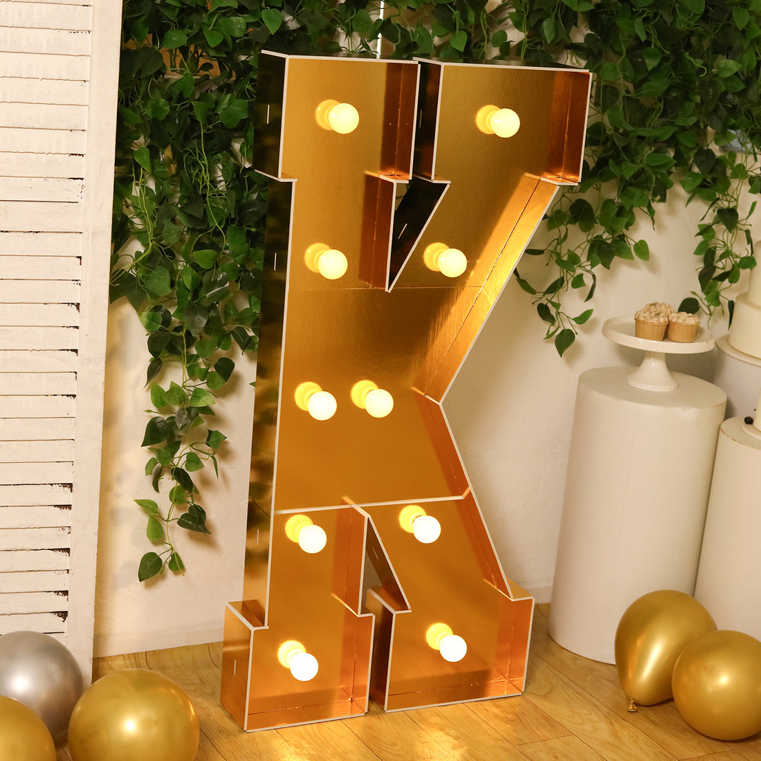 Gold marquee letter 'K' with lights, styled in a festive setting.