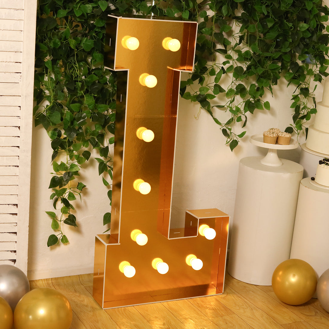 Gold marquee letter "L" with lights in a festive setting.
