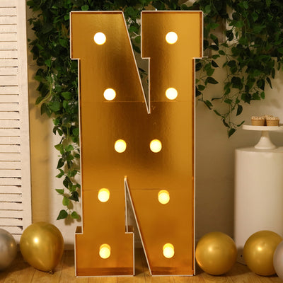 Gold letter "N" marquee sign with lights in a festive setting.