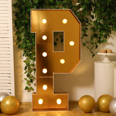 Gold marquee letter "P" with lights, surrounded by greenery and balloons.