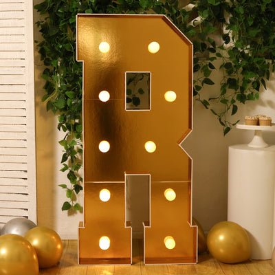 Gold marquee letter "R" with lights, surrounded by balloons and greenery.