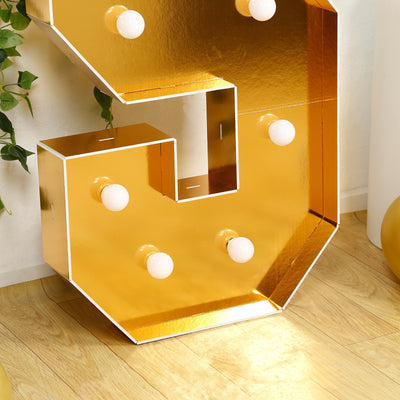 Gold marquee letter "S" with light bulbs on a wooden floor.