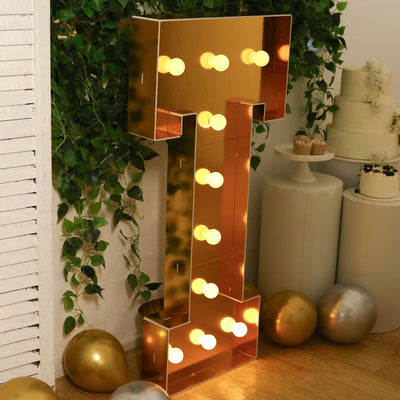 Gold marquee letter "T" with lights, decorated with balloons and cake backdrop.