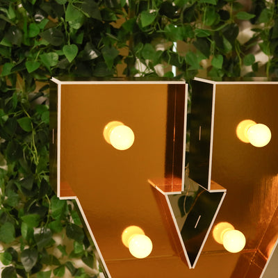 Decorative marquee letter with bulbs against a green leafy background.