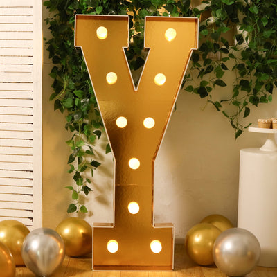 Gold marquee letter "Y" with lights, surrounded by balloons and greenery.