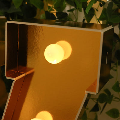 Gold marquee number seven with light bulbs, reflecting ambient greenery.