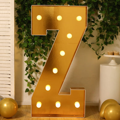 Gold marquee letter "Z" with lights, surrounded by greenery and balloons.