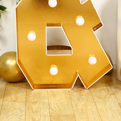 Gold marquee letter "R" with light bulbs on a wooden floor.