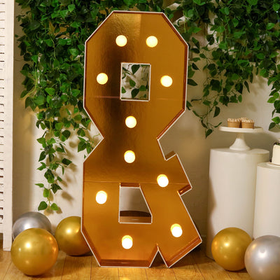 Gold marquee ampersand sign with lights in a festive setting.
