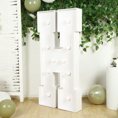White letter "H" marquee sign with lights, set against greenery and balloons.