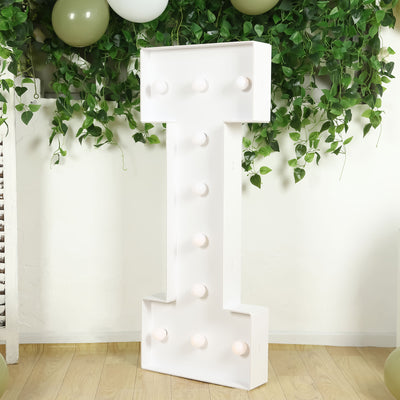 White marquee letter "I" with lights against greenery backdrop.