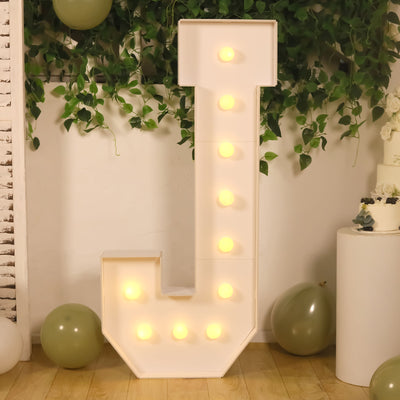 Light-up marquee letter "J" with bulbs, styled with greenery and balloons.