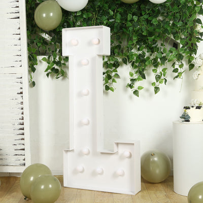 White marquee letter "I" with lights, surrounded by greenery and balloons.