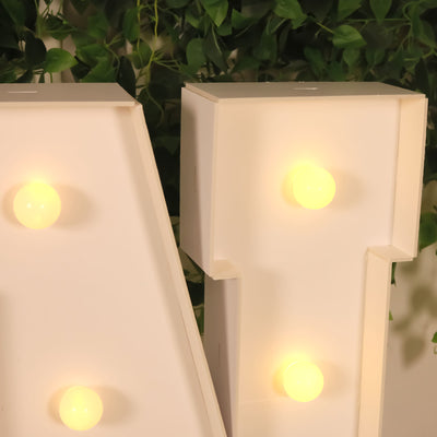 Light-up marquee letters with glowing bulbs against greenery backdrop.