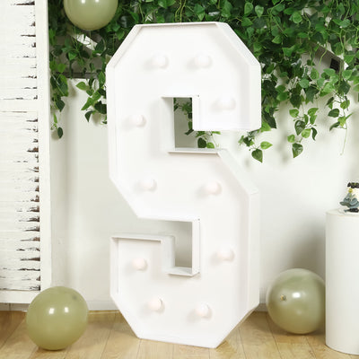 Large white marquee letter "S" with bulbs, surrounded by greenery and balloons.