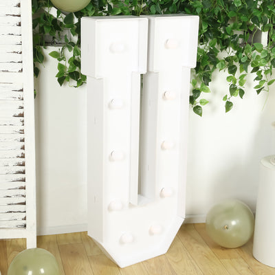 White marquee letter "J" with light bulbs against greenery backdrop.