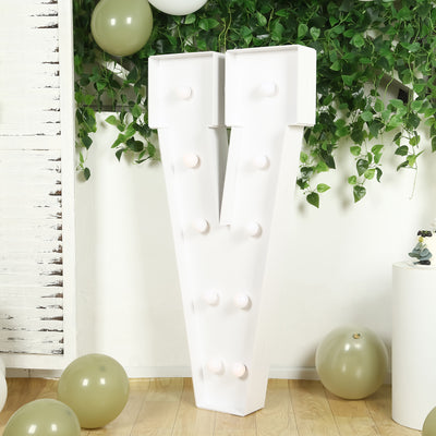 Large decorative letter "V" with light bulbs, surrounded by greenery and balloons.