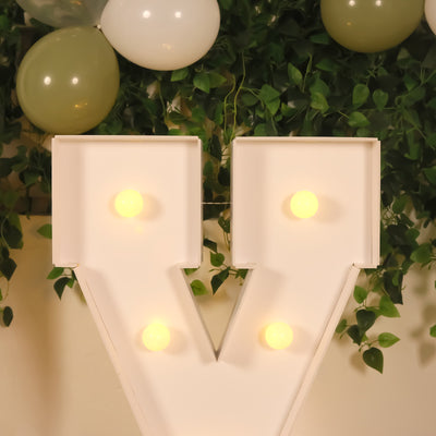 Vintage light-up letter "V" with bulbs, decorated with green balloons and foliage.
