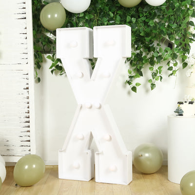 White marquee letter X against greenery and balloons in a festive setting.