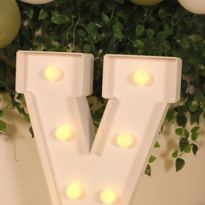 Marquee letter "V" with lights, surrounded by greenery.