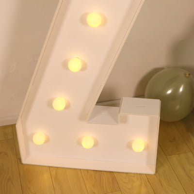 Illuminated decorative letter "L" with bulbs on a wooden floor.