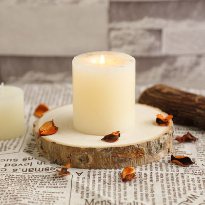 White candle on a wooden slice surrounded by dried petals and newspaper backdrop.