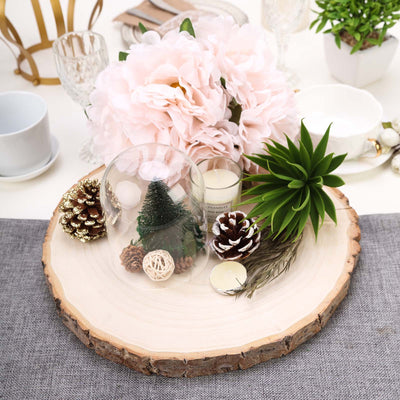 Decorative centerpiece with flowers, candles, and natural elements on a wooden platter.