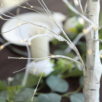 Decorative white tree branches with fairy lights for elegant table settings.