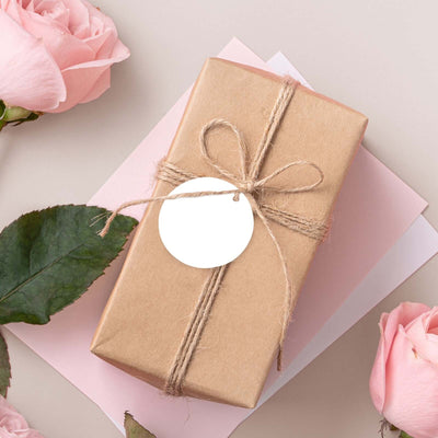Brown gift box with twine and tag, surrounded by pink roses and papers.