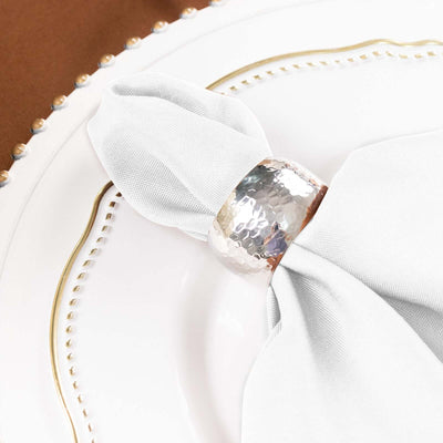 Silver hammered napkin ring on a white plate with a light cloth napkin.